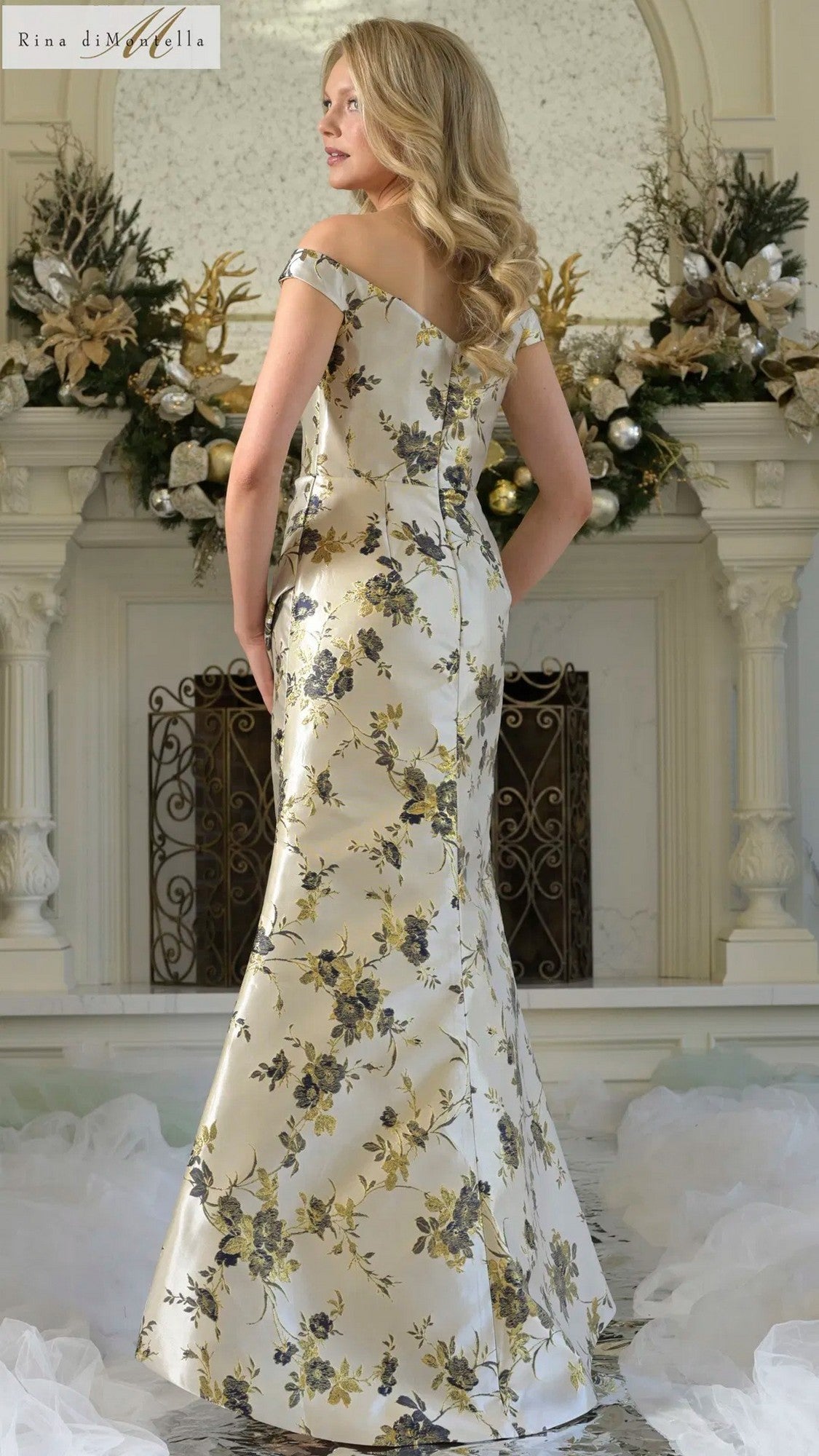 A woman in a Rina Di Montella RD3350 long formal dress poses before a festive fireplace decorated with holiday greenery and ornaments.